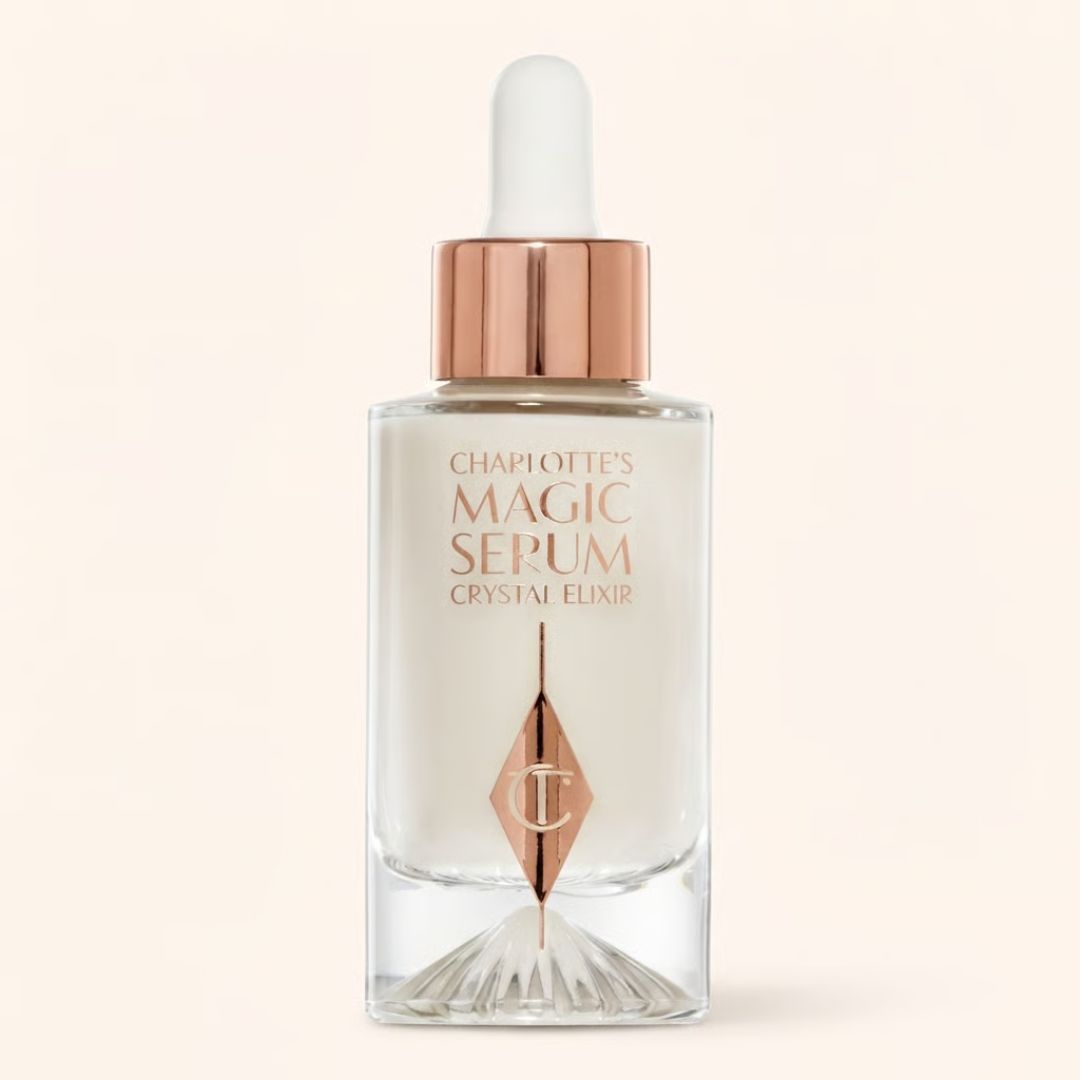 Charlotte's Magic Serum Crystal Elixir in a clear glass dropper bottle with a rose gold collar and white dropper cap, set against a solid pale beige background.