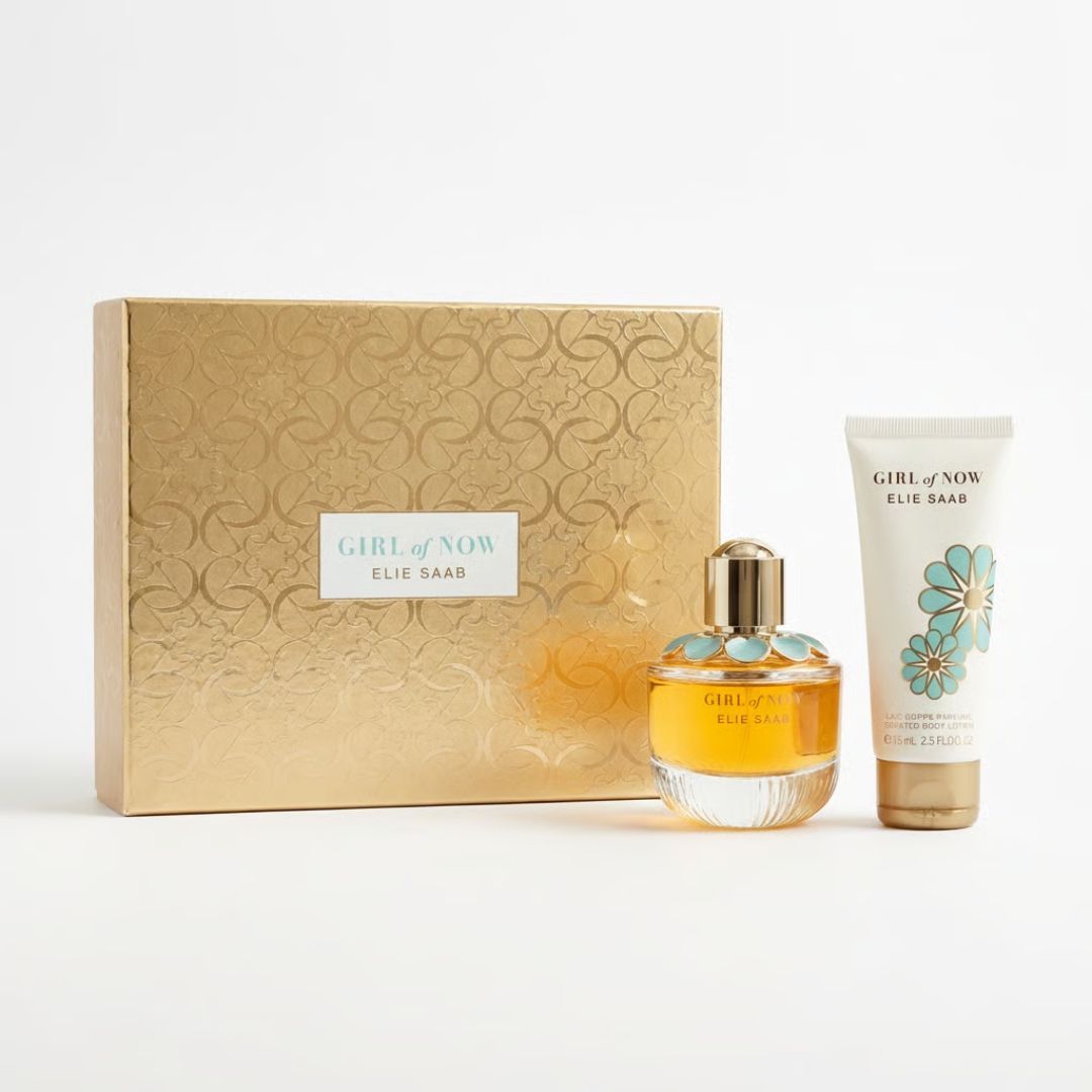 Elie Saar Girl of Now fragrance gift set featuring a gold patterned box, a clear glass perfume bottle filled with amber liquid, and a white body care tube with teal floral graphics.