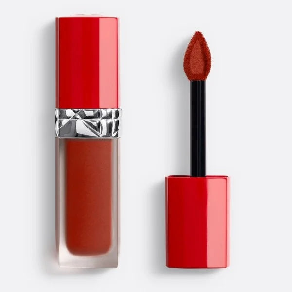 A liquid lipstick in a clear tube showing a warm terracotta brown shade, next to its applicator wand with a red cap, on a light gray background.